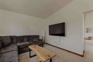 Ein Wohnzimmer mit Ecksofa, Couchtisch aus Holz, Wandfernseher und einem kleinen Beistelltisch.