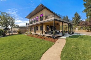 Ein zweistöckiges Haus mit überdachter Terrasse, umzäunter Garten und kleiner Gartenhütte.