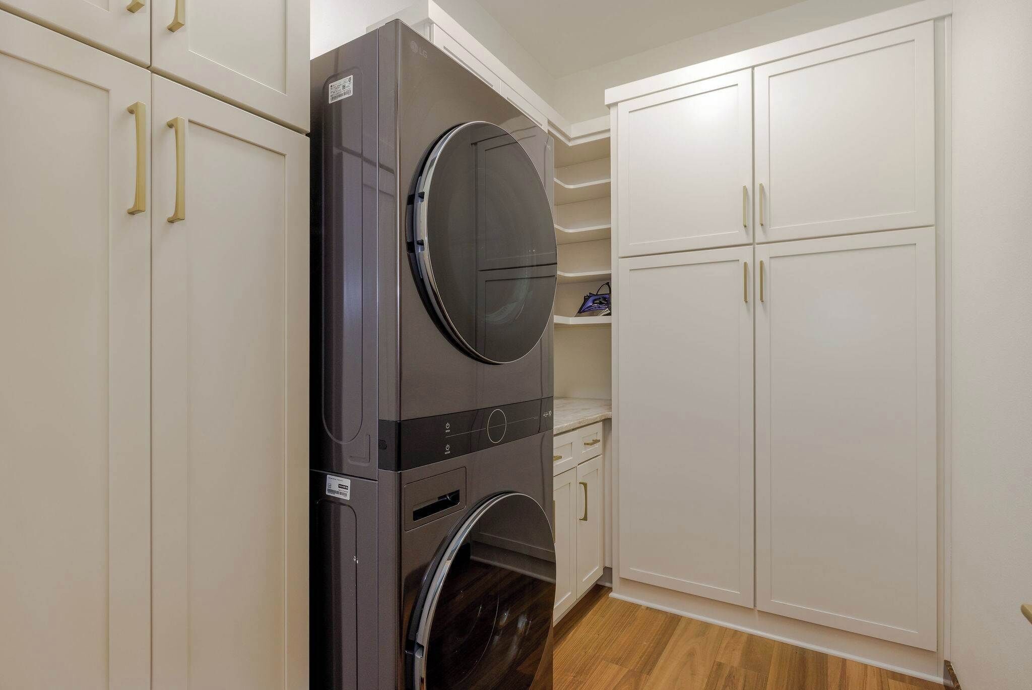 A compact laundry room with a built-in washer and dryer, white cabinetry, and a small shelf.