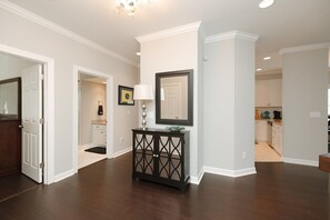 A hallway with a dark wooden floor, white walls, and a black console table with a lamp. - Waterfront Slice of WB Paradise w Dock and Boat Lift! PRIME location! (Wrightsville Beach)