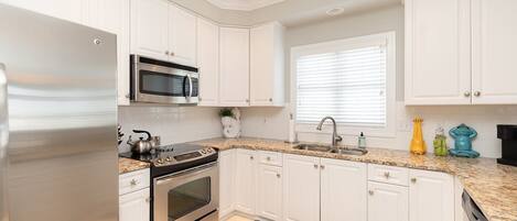 A kitchen with white cabinets, stainless steel appliances, a granite countertop, and a window with blinds.
