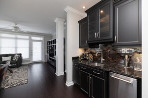 A modern kitchen with dark cabinetry, a stainless steel sink, and a black countertop. - Waterfront Slice of WB Paradise w Dock and Boat Lift! PRIME location! (Wrightsville Beach)