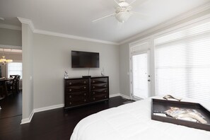 A bedroom with a bed, dresser, television, and a door with blinds. - Waterfront Slice of WB Paradise w Dock and Boat Lift! PRIME location! (Wrightsville Beach)