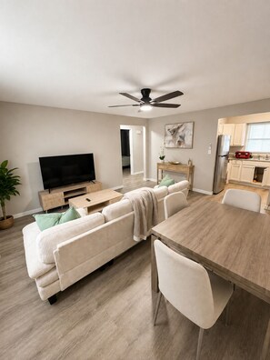 A modern living room with a sofa, a TV, a dining table, and a kitchen area. - Terrific 2-bedroom apartment with AC in sunny Tampa (Tampa)