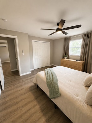 Un dormitorio con cama, ventilador de techo, ventana con cortinas y puerta que da a otra habitación.