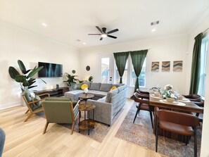 A modern living room with a grey sofa, wooden coffee table, and a dining area with a wooden table set for six. - Spacious 4-bedroom house in quaint Houston with AC and gym access (Houston)