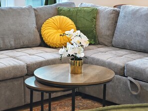 A sectional sofa with a round wooden coffee table and a gold vase with white flowers. - Spacious 4-bedroom house in quaint Houston with AC and gym access (Houston)