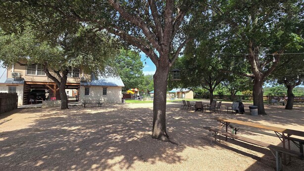 Un parque al aire libre con mesas de picnic, una zona de estar techada y un parque infantil al fondo.