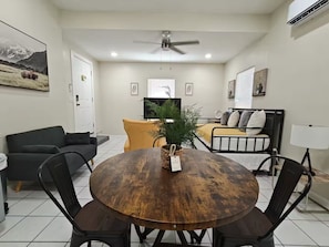A living room with a round wooden table, black chairs, a sofa, a bed, and a ceiling fan. - Bugambilias Apartment (Laredo)