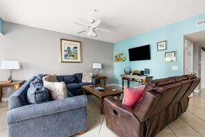 Ein Wohnzimmer mit einem blauen Sofa, einem braunen Ledersessel, einem Holztisch und einem Deckenventilator.