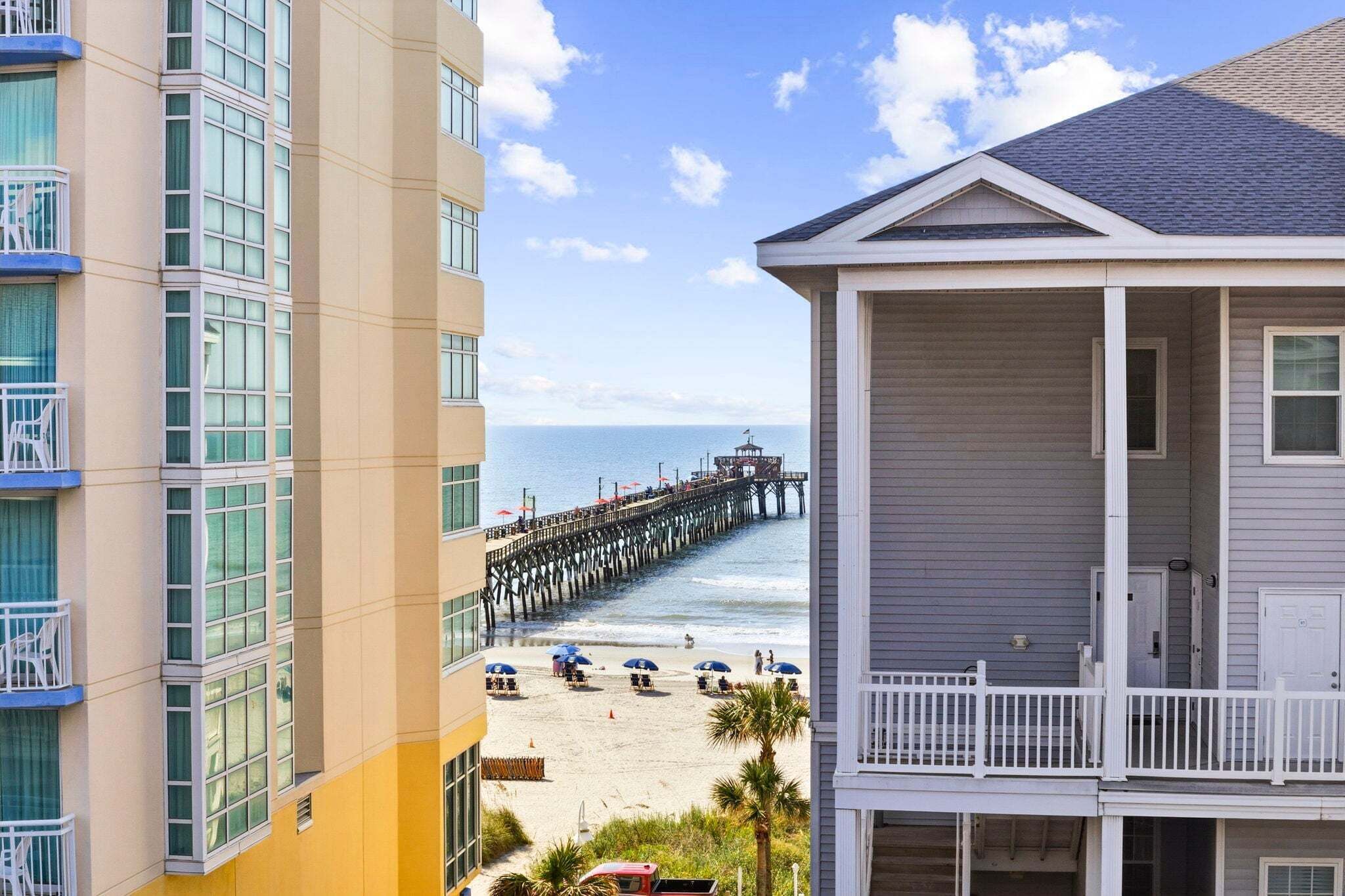 A beachfront property with a pier extending into the ocean, a balcony with a view of the beach, and a building with multiple windows.