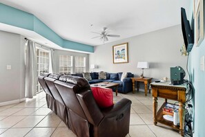 A living room with a brown leather sofa, a blue couch, a wooden coffee table, and a ceiling fan. - Six on the Beach - Spacious 6BR Condo w/ Shared Pool and Hot Tub (Sleeps 12) (North Myrtle Beach)