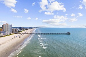 A beach with a pier extending into the ocean, buildings along the shore, and clear skies. - Six on the Beach - Spacious 6BR Condo w/ Shared Pool and Hot Tub (Sleeps 12) (North Myrtle Beach)
