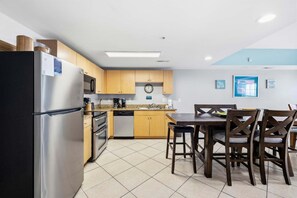 A modern kitchen with stainless steel appliances, wooden cabinets, and a dining area with a table and chairs. - Six on the Beach - Spacious 6BR Condo w/ Shared Pool and Hot Tub (Sleeps 12) (North Myrtle Beach)