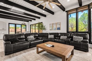 A modern living room with a sectional sofa, a wooden coffee table, and large windows offering a view of the outdoors. - Sandia Vista Retreat 5 BDR 4.5 Bathroom, Hot Tub, Game Room (Albuquerque)
