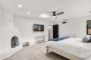 A bedroom with a bed, a ceiling fan, a wall-mounted TV, and a door leading to another room. - Sandia Vista Retreat 5 BDR 4.5 Bathroom, Hot Tub, Game Room (Albuquerque)