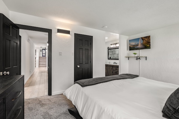 A bedroom with a bed, dresser, and a hallway leading to a staircase.