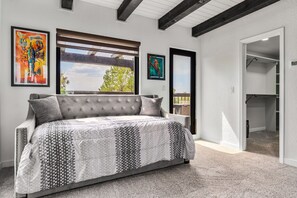 A bedroom with a large bed, a window with blinds, and artwork on the walls.