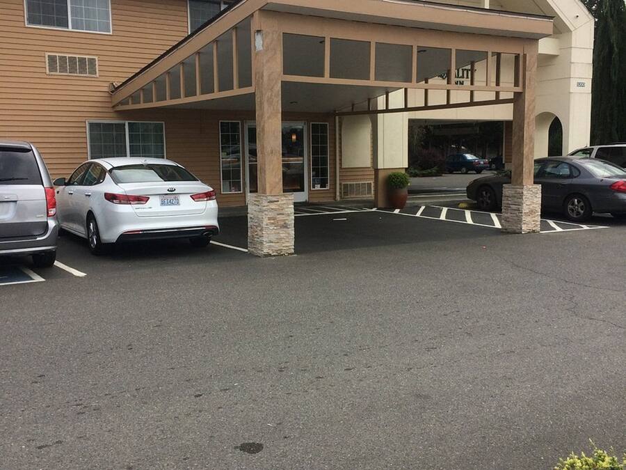Entrada de hotel con área de estacionamiento techada, un edificio de fachada color crema y una fila de coches aparcados.
