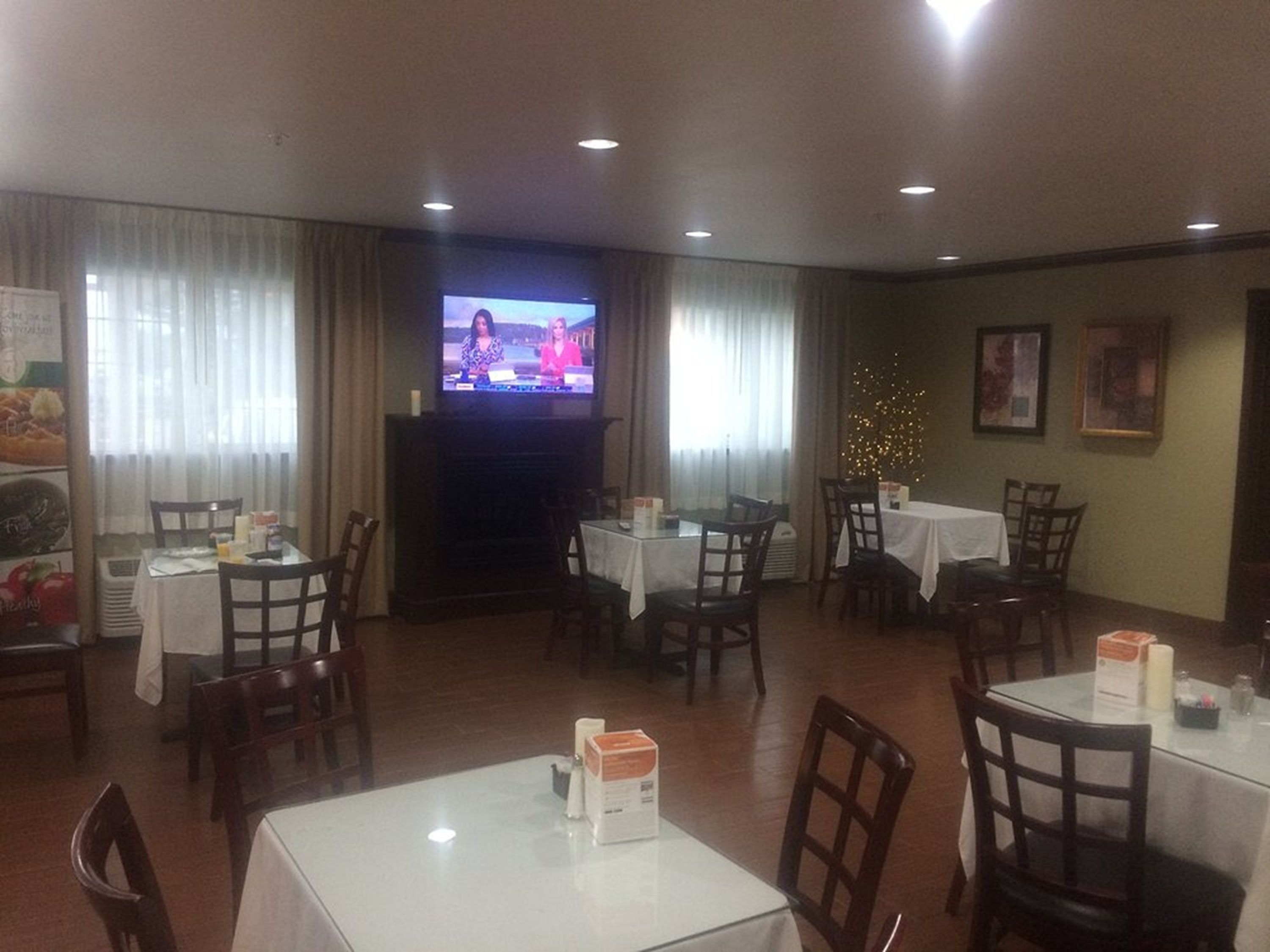 A restaurant with multiple tables and chairs, a television screen, and a Christmas tree decoration.