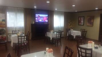 A restaurant with multiple tables and chairs, a television screen, and a Christmas tree decoration.