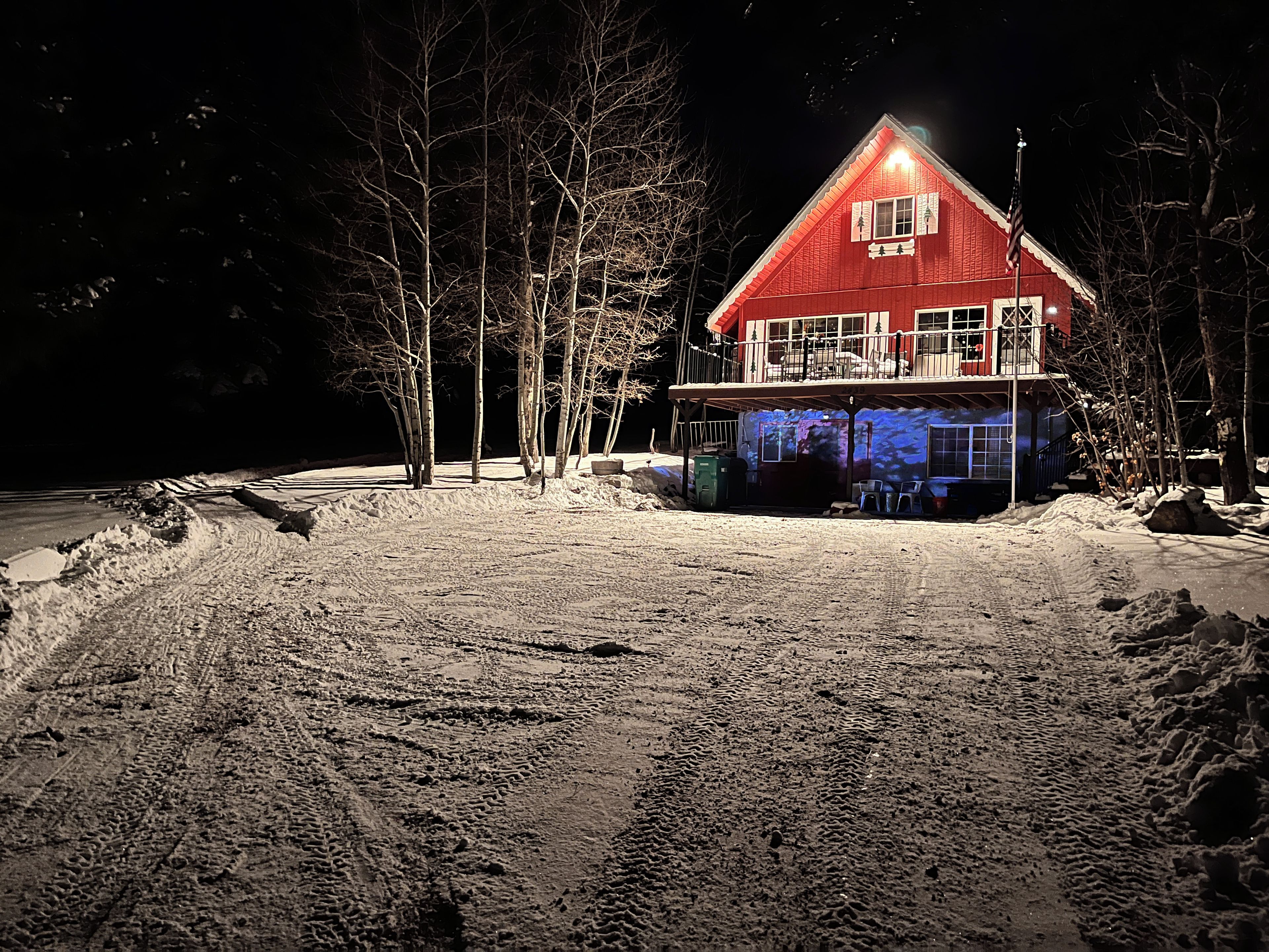 A two-story house with a red exterior, a balcony, and a snow-covered ground.