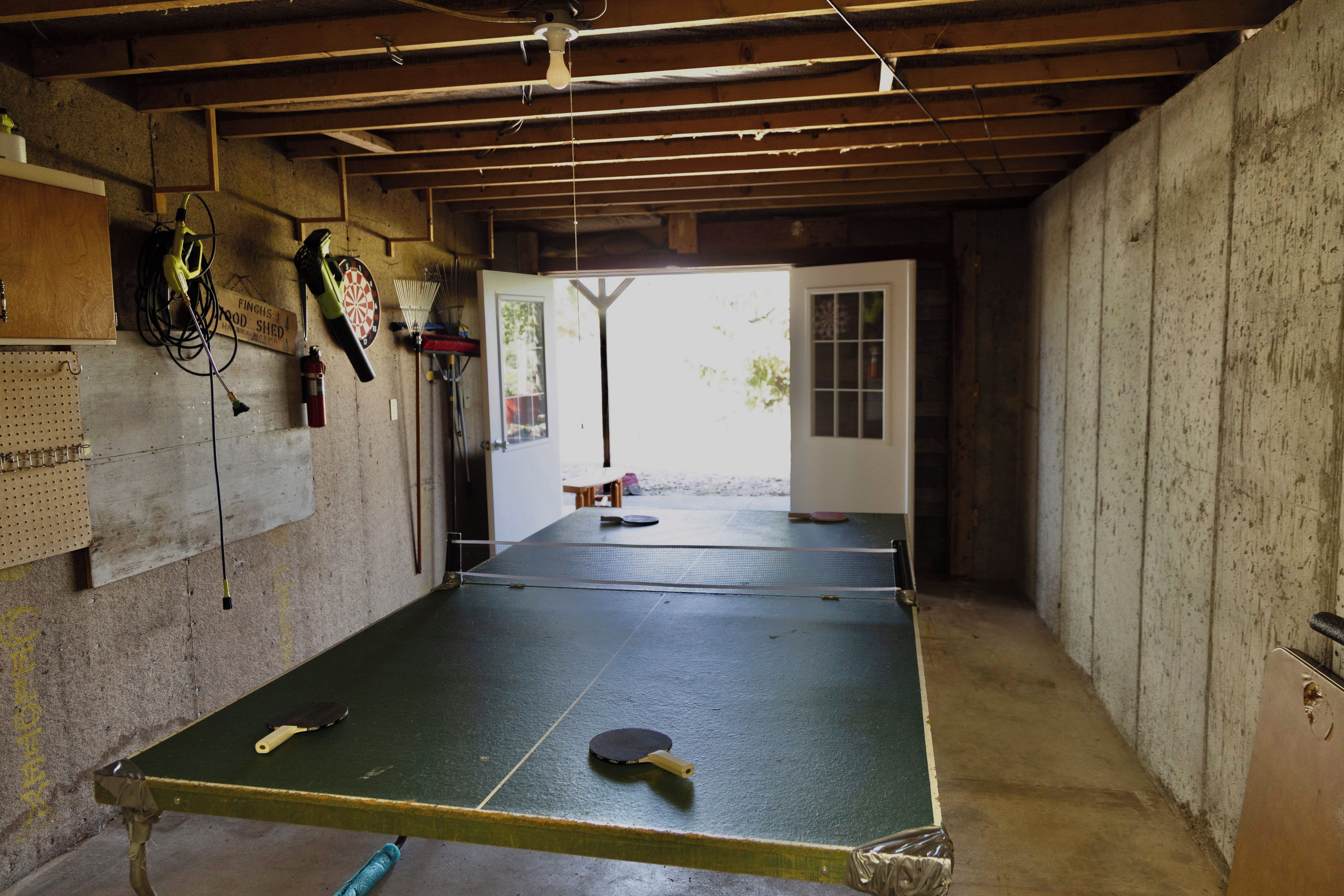 Une table de ping-pong dans une pièce dont le plafond est en bois, avec un jeu de fléchettes et un extincteur accroché au mur.