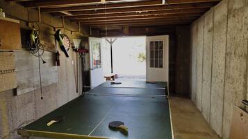 Une table de ping-pong dans une pièce dont le plafond est en bois, avec un jeu de fléchettes et un extincteur accroché au mur.