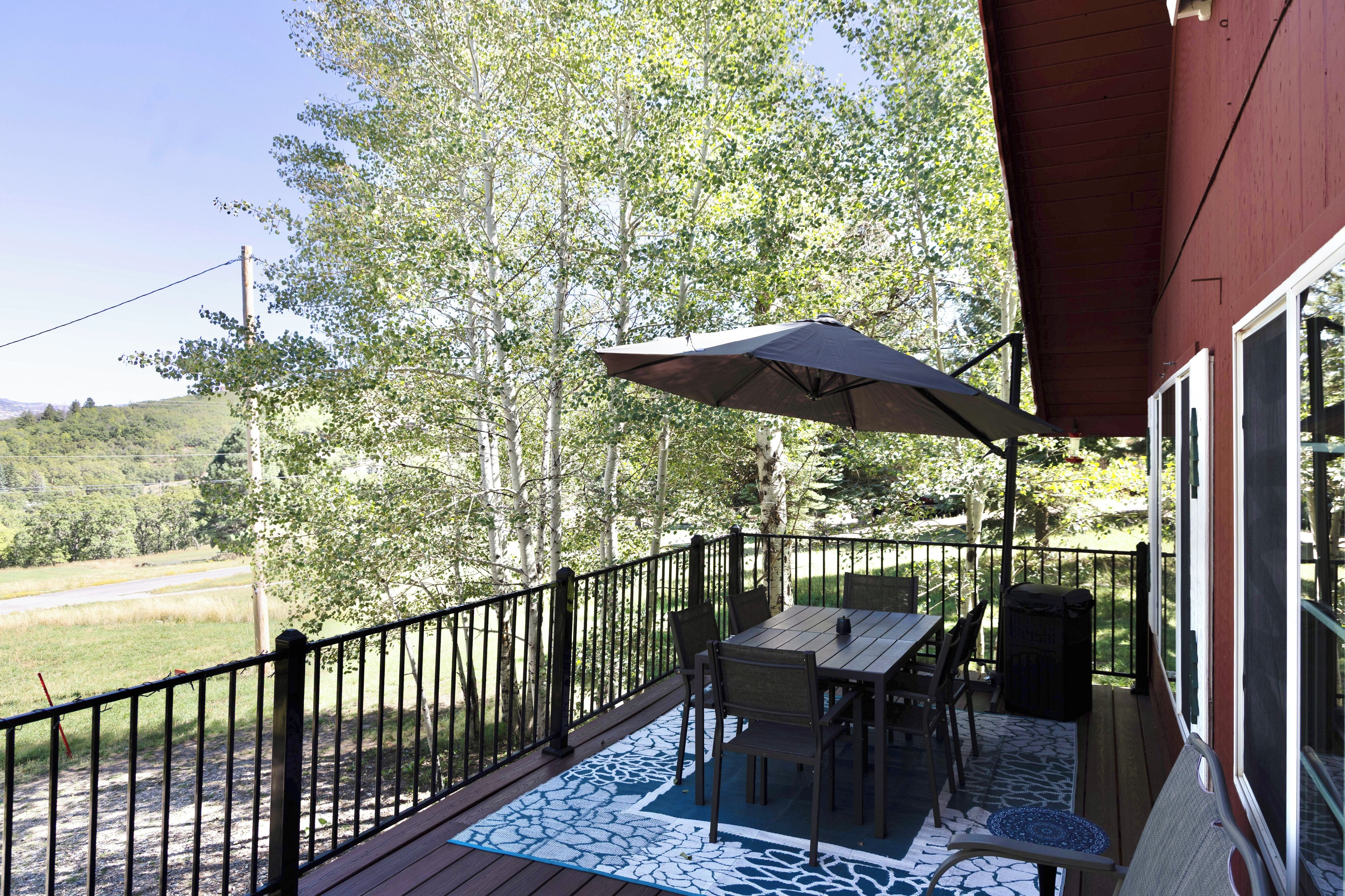Une terrasse avec une table et des chaises, un parasol, et une vue sur les arbres et une route.