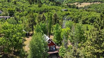 Une maison rouge, entourée d’une forêt dense, sous un ciel dégagé.