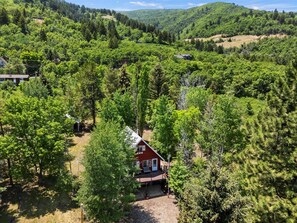 A red house surrounded by dense forest, with a clear sky above.