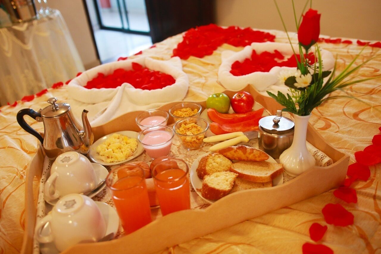 A breakfast tray with various food items and drinks, a teapot, and a vase with flowers.