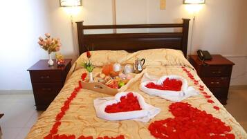 Una cama con pétalos de rosa, un servicio de comidas y un florero con flores.