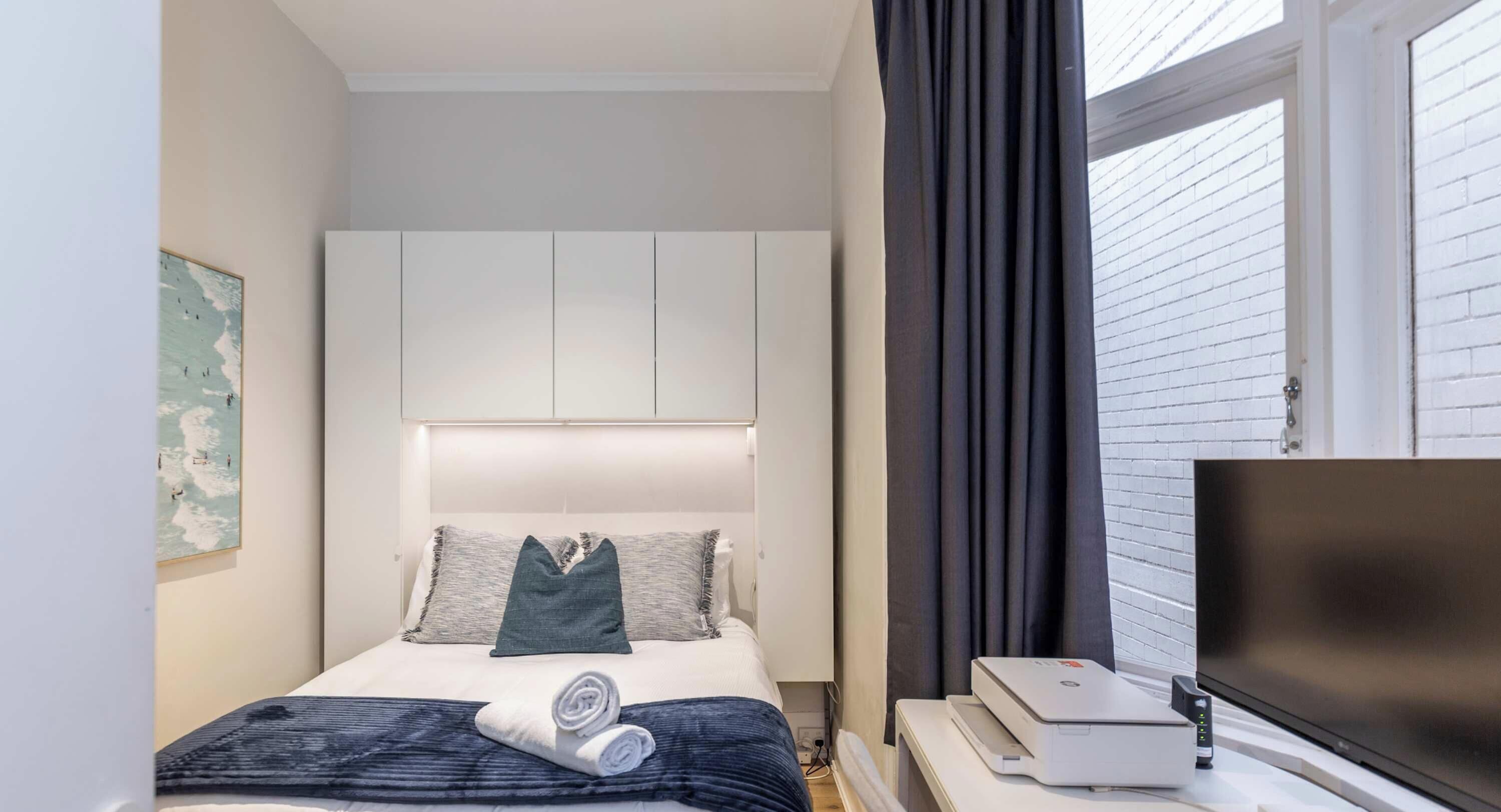 A hotel room with a bed, a flat-screen TV, a printer, and a window with curtains.