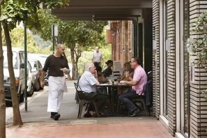 An outdoor dining area with tables and chairs, a waiter walking by, and a building with a brick facade in the background. - Art Deco 2BR Retreat in the Heart of Potts Point (Potts Point)