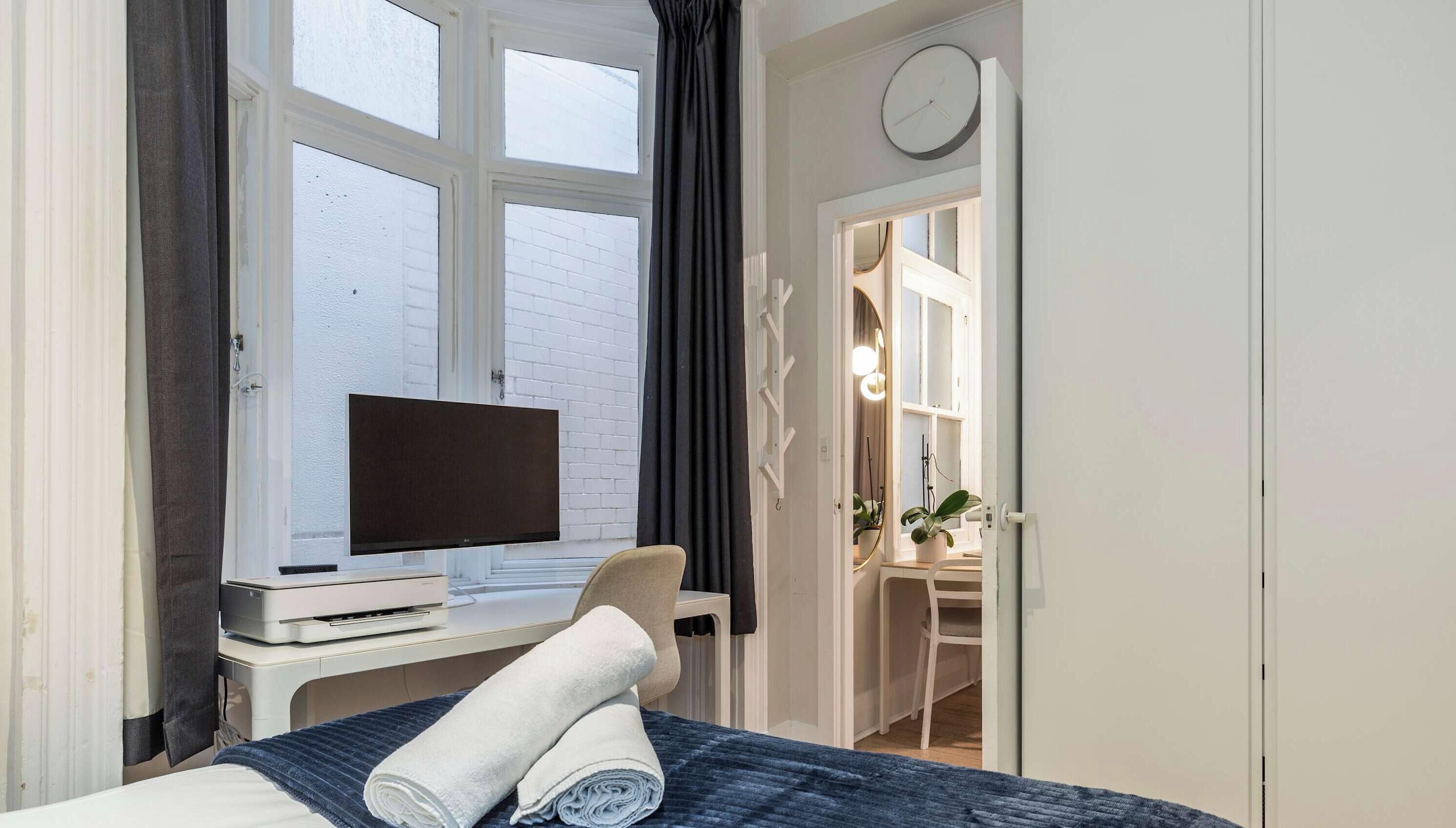 Een hotelkamer met een bed, een bureau met een flatscreen televisie, een raam met gordijnen, en een deur naar een badkamer.