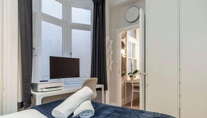 A hotel room with a bed, a desk with a flat-screen TV, a window with curtains, and a door leading to a bathroom. - Art Deco 2BR Retreat in the Heart of Potts Point (Potts Point)