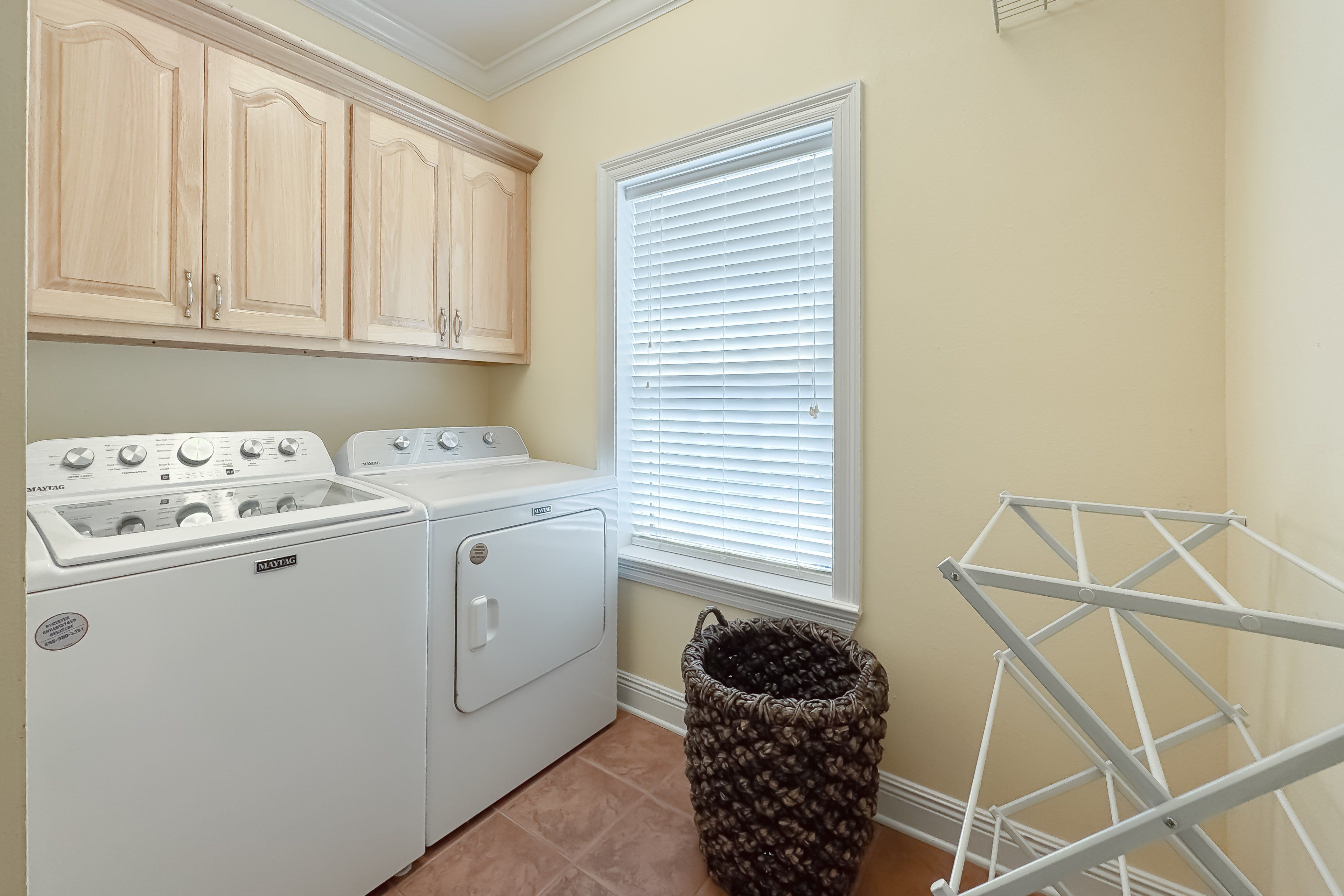 Un cuarto de lavado con lavadora y secadora Maytag, un tendedero y una ventana con persianas.