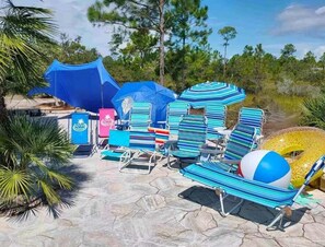 Sitzgelegenheit im Freien mit gestreiften Stühlen, einem blauen Sonnenschirm, einem Strandball und einem Zelt.
