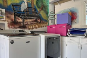 A laundry room with a Maytag washer and dryer, a Whirlpool dishwasher, and a colorful mural on the wall. - The Blue Manor at Herons Walk | Outdoor Pool | 4 Kayaks | My Beach Getaways (Pensacola)