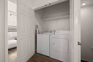 A laundry room with a washing machine and dryer, a door leading to a bedroom, and a ceiling light fixture. - Urban Oasis in Downtown Austin (Austin)