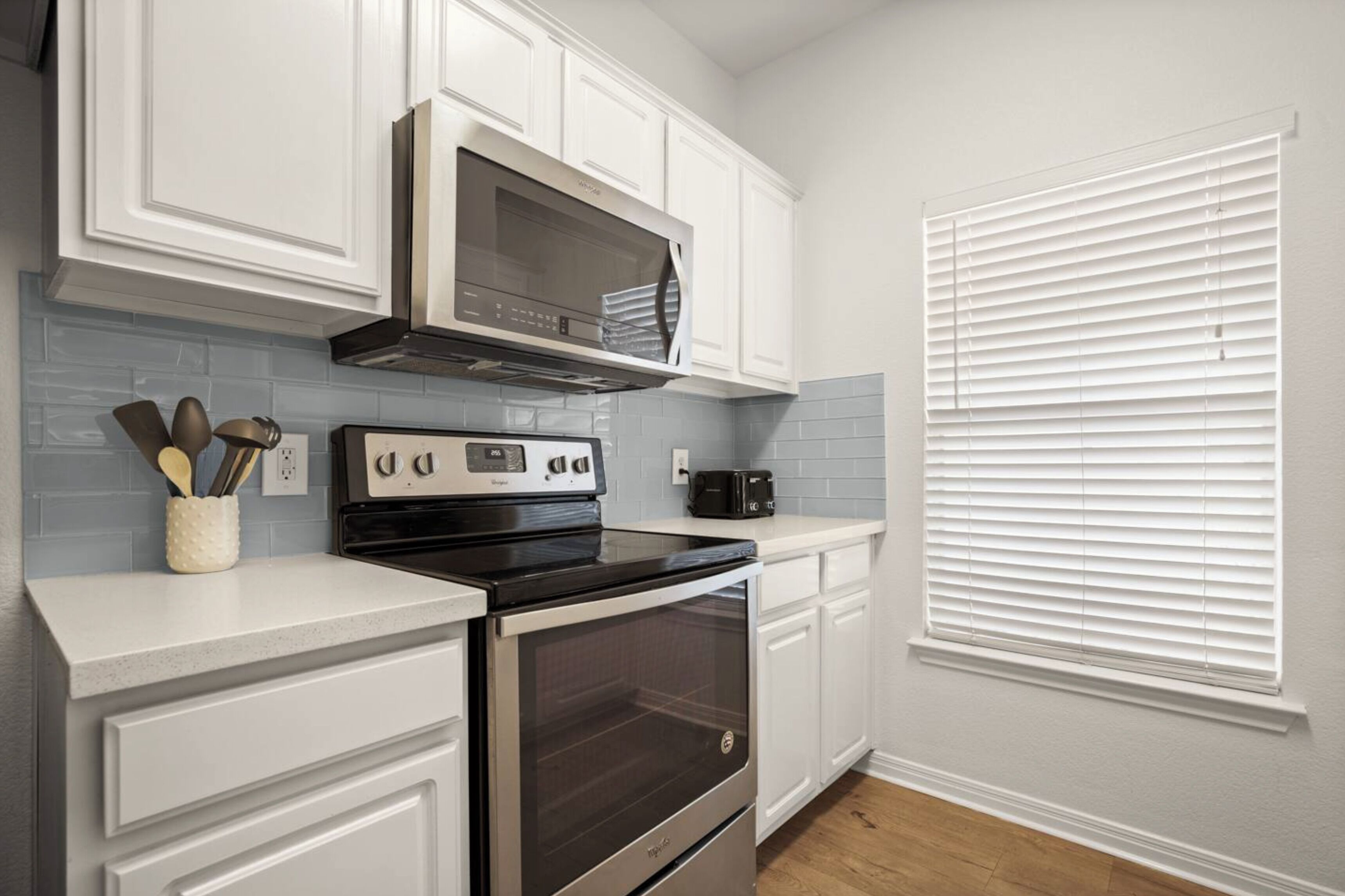 A kitchen with white cabinetry, a stainless steel range hood, a black oven, and a toaster on the countertop.