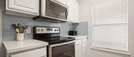 A kitchen with white cabinetry, a stainless steel range hood, a black oven, and a toaster on the countertop.