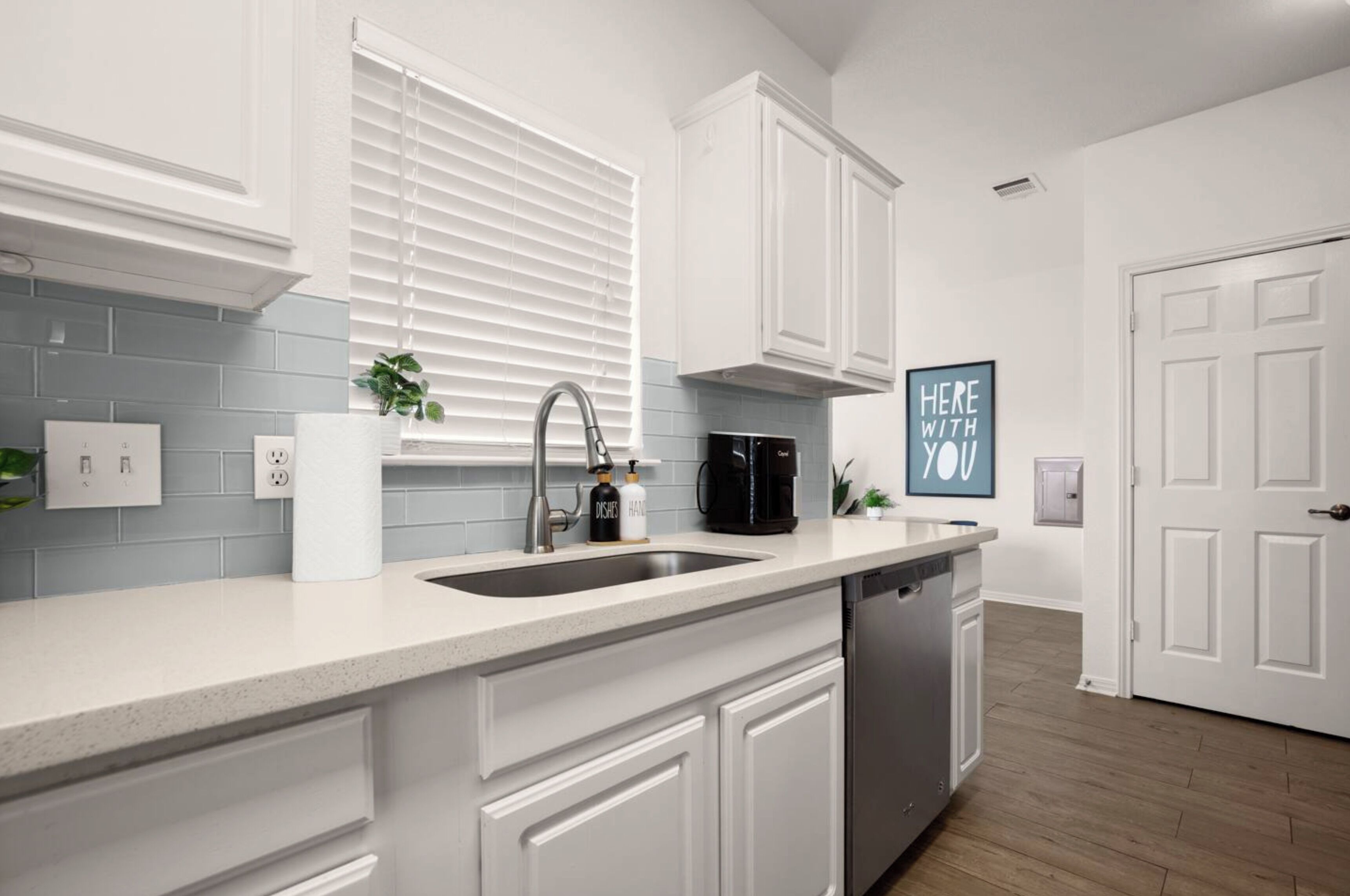 A modern kitchen with white cabinetry, a double sink, a coffee maker, and a dishwasher.