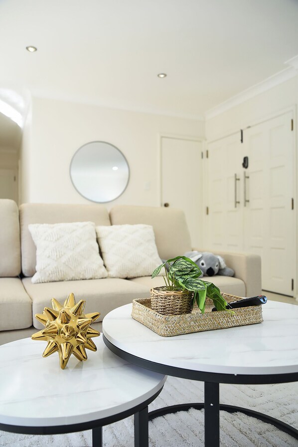 A modern living room with a sofa, two round tables, a decorative gold object, and a woven basket with a plant.
