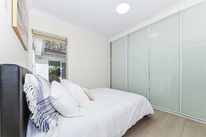 A bedroom with a bed, a bedside table, a wardrobe, and a window.