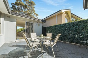 A patio with a table and chairs, a sliding glass door, and a hedge. - Bright 4BR Pool Retreat | Maquarie Park & Eastwood (Marsfield)