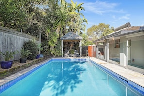 A swimming pool with a tiled edge, surrounded by a wooden fence and potted plants.