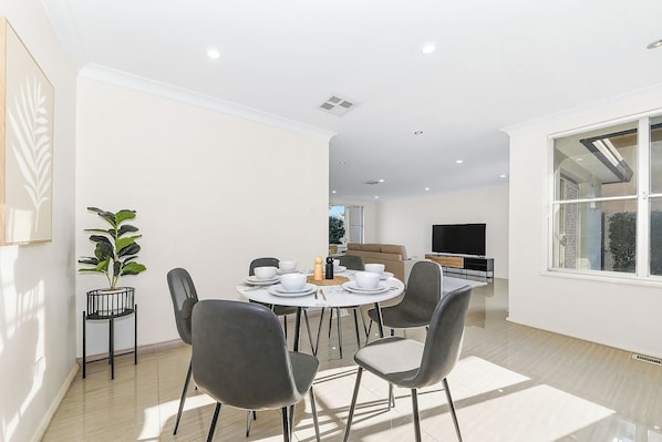 A modern dining area with a round table, chairs, and a television in the background.