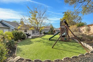 A residential area with a well-maintained lawn, a swing set, and a house with a visible chimney. - 4BR Family Getaway  Private Office, Playground & Backyard (Thousand Oaks)